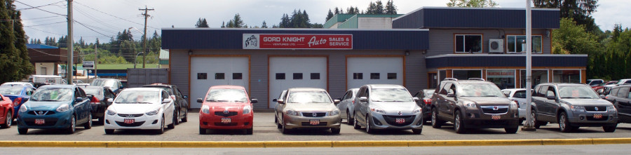 Row of pre-owned cars and suvs in front of a 3-bay garage. Auto sales office on right side.